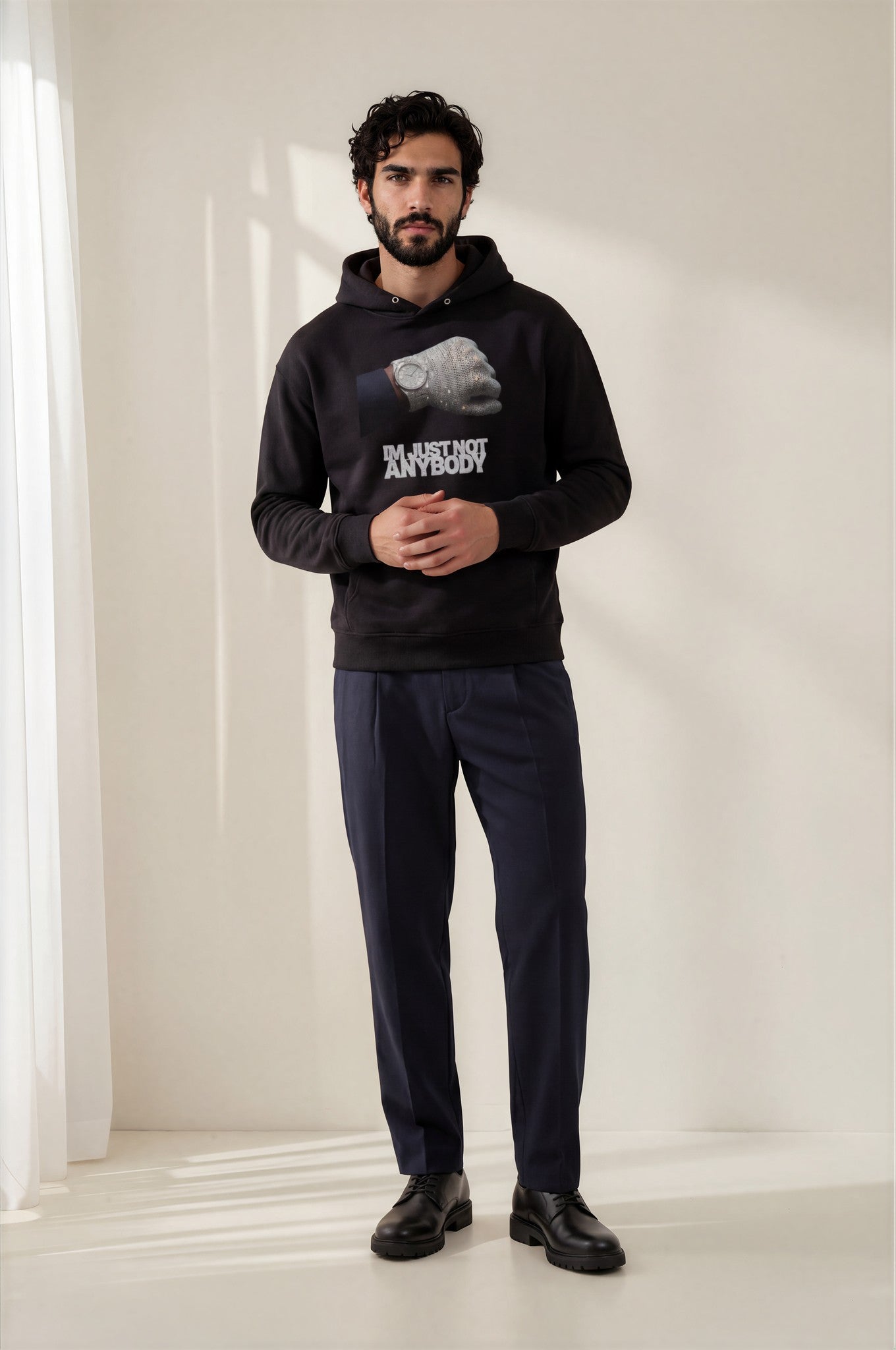 Man wearing a black hoodie with graphic design and text, standing against a plain white background